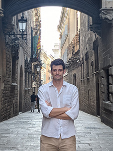 An image of Marko Mićić posing with his arms crossed in a old European looking, narrow cobblestone roadway.