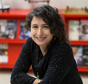 An image of Sera Markoff sitting at a table in front of a bookcase.